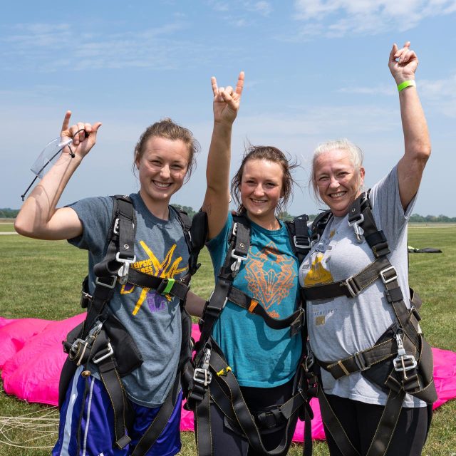 Three women point to the sky after landing from a tandem skydive with Start Skydiving