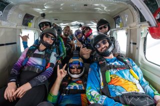 Group of licensed jumpers pose for the camera with smiles and various hand signals on the plane.