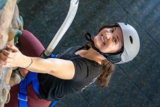 Woman leans back and smiles while climbing on the indoor climbing wall at Start Skydiving