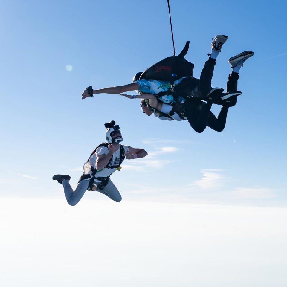 Outside perspective of a tandem skydiving pair with their videographer flying alongside them.