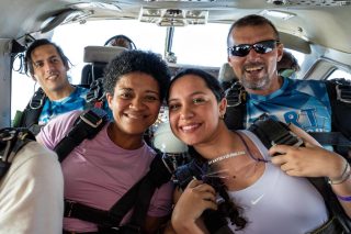 Two female tandem students lean together for a photo on the plane preparing for their jump.