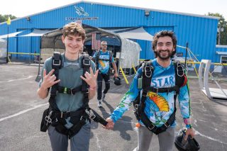 Tandem instructor leads his student to the airplane by holding on to his harness.