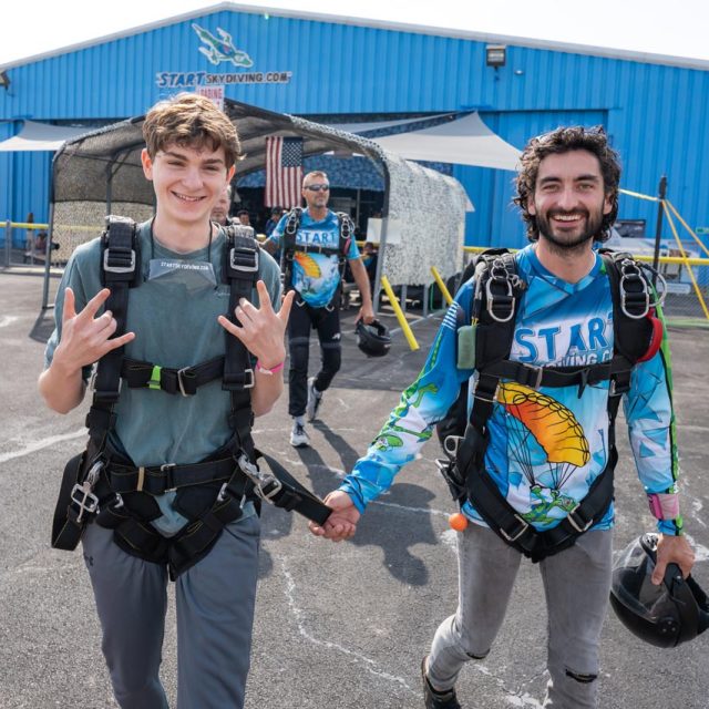 Tandem instructor leads his student to the airplane by holding on to his harness.