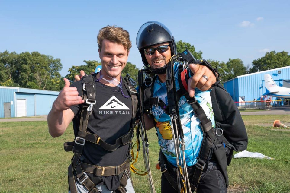 Male tandem skydiving student and instructor pose together after their jump.