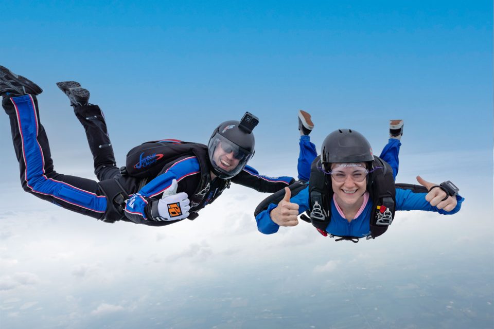 Skydiving student and her instructor give a thumbs up to the camera during freefall.