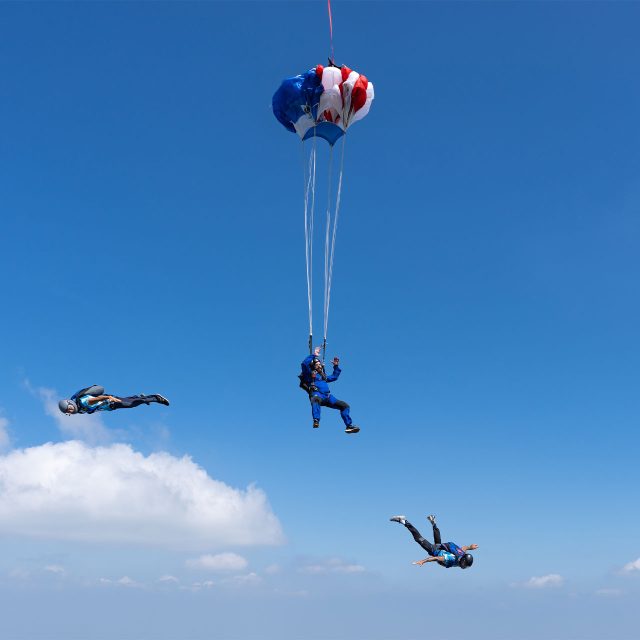 AFF instructors tracking away from an AFF student after deployment as the student's red white and blue parachute opens