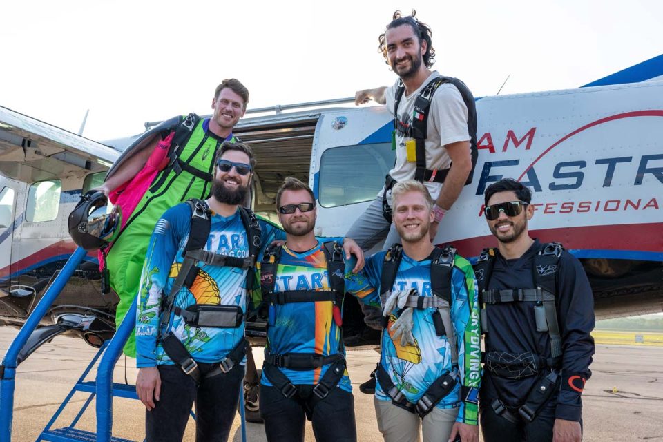 Group of male skydivers pose before boarding the plane for a jump.