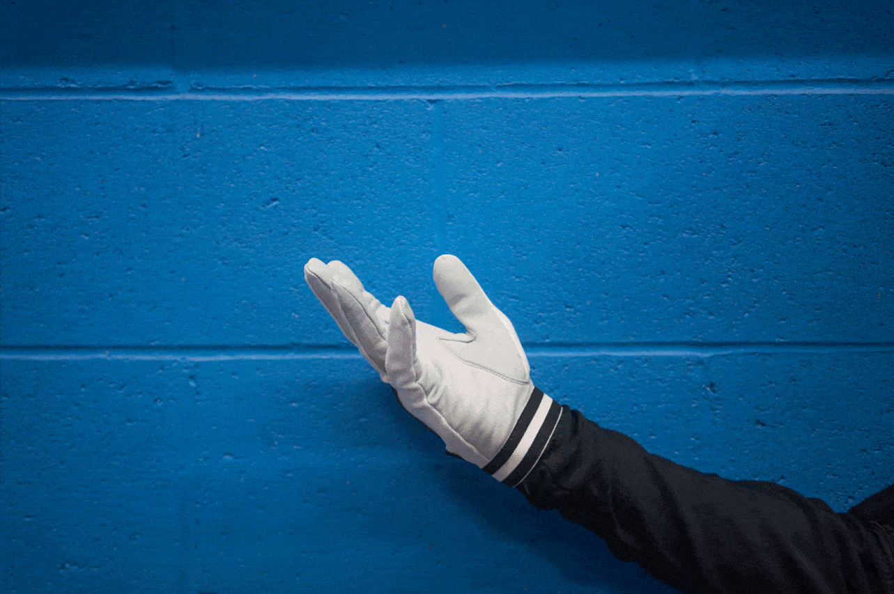 Hand wearing a white glove giving the open pilot chute signal against a blue background.