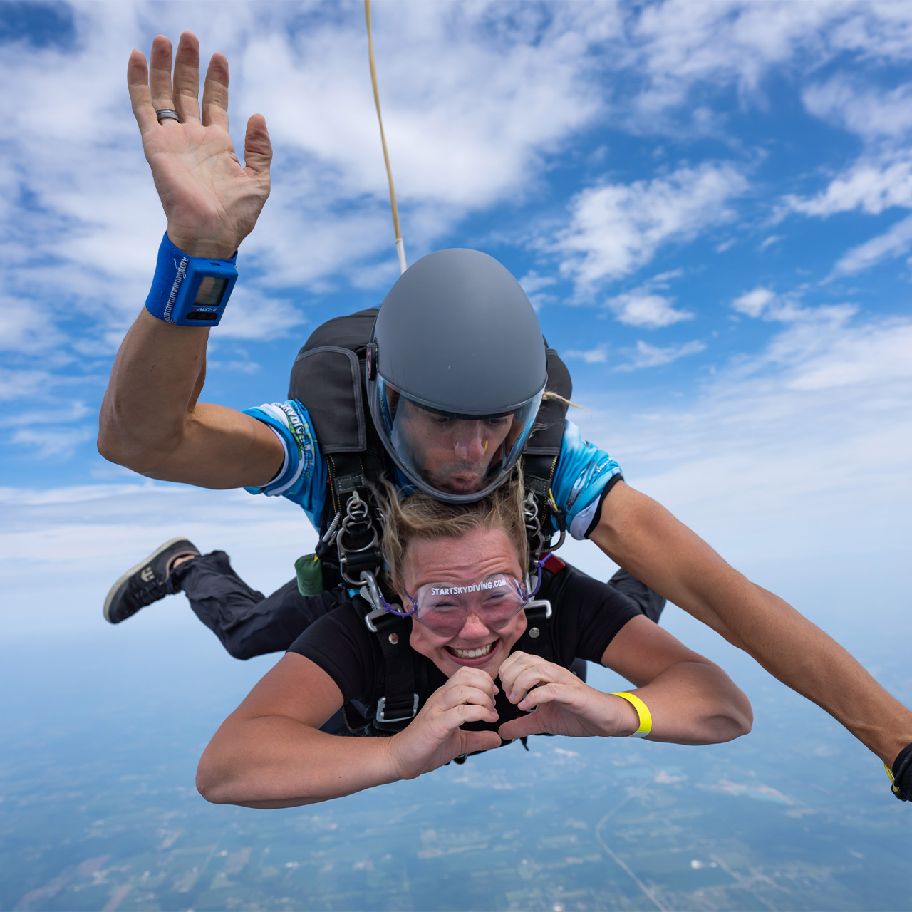 Blonde female tandem student forming a heart with her hands as she freefalls on a tandem skydive at Start Skydiving