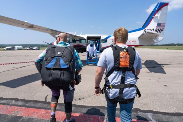 Male tandem skydiving student and instructor walk toward the airplane.