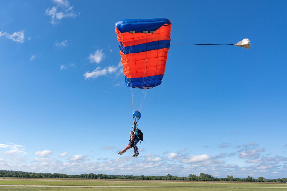 Tandem skydivers land a blue and orange parachute.