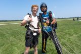 Male tandem skydiving pair post after their jump - instructor gives thumbs up while student give shaka symbol.
