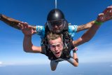 Tandem skydiver with arms outstretched and his instructor smile big at the camera.