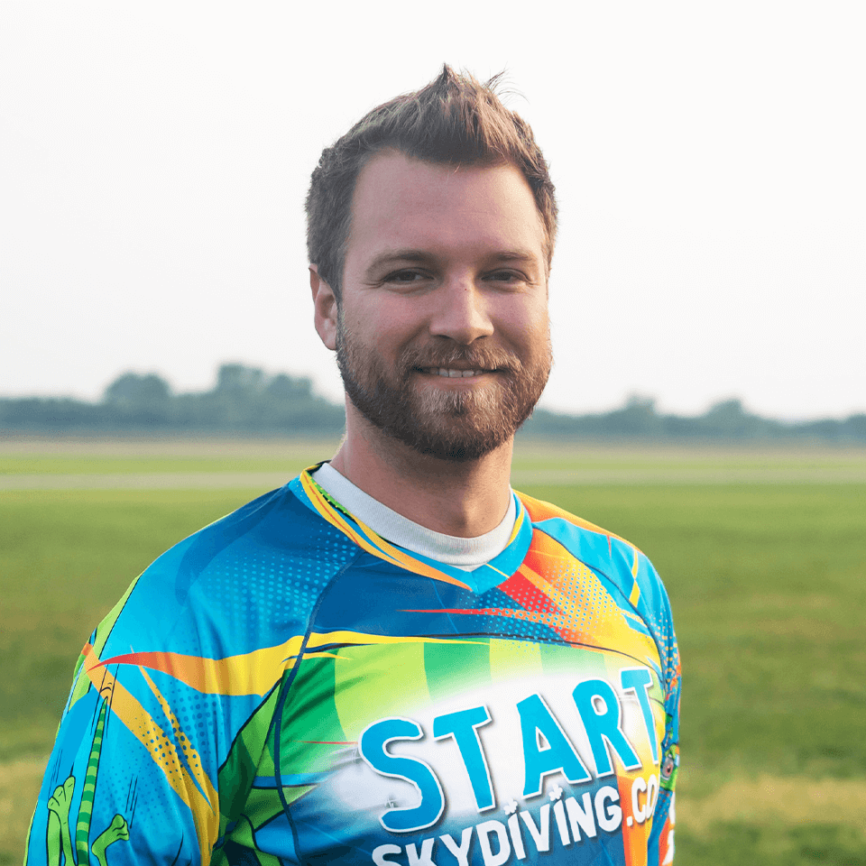 Light brown-haired male instructor and DropZone Owner Alex Hart wearing StartSkydiving.com team jersey.