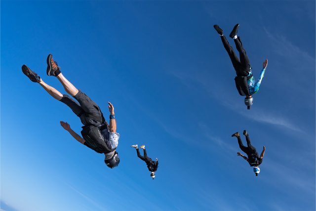 A group of licensed skydivers flying at an angle through the sky