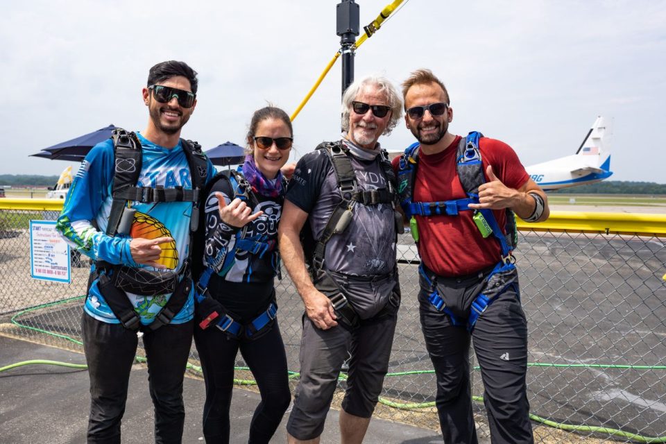 A group of skydivers wearing their sport skydiving rigs pose for a photo