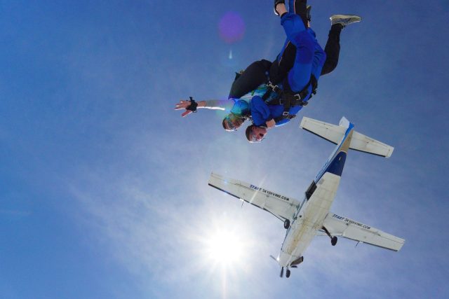 Tandem skydiving pair with an airplane and sun in the background