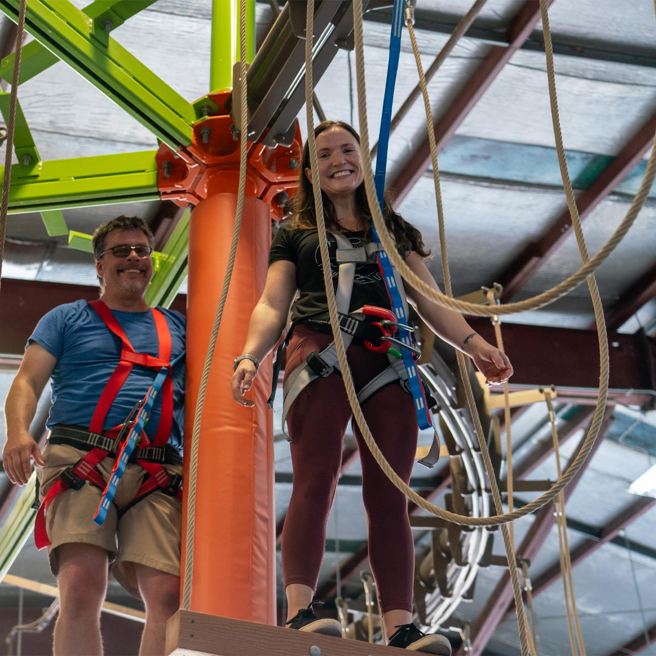 A smiling woman and a grinning man completing the indoor ropes course at Start Skydiving