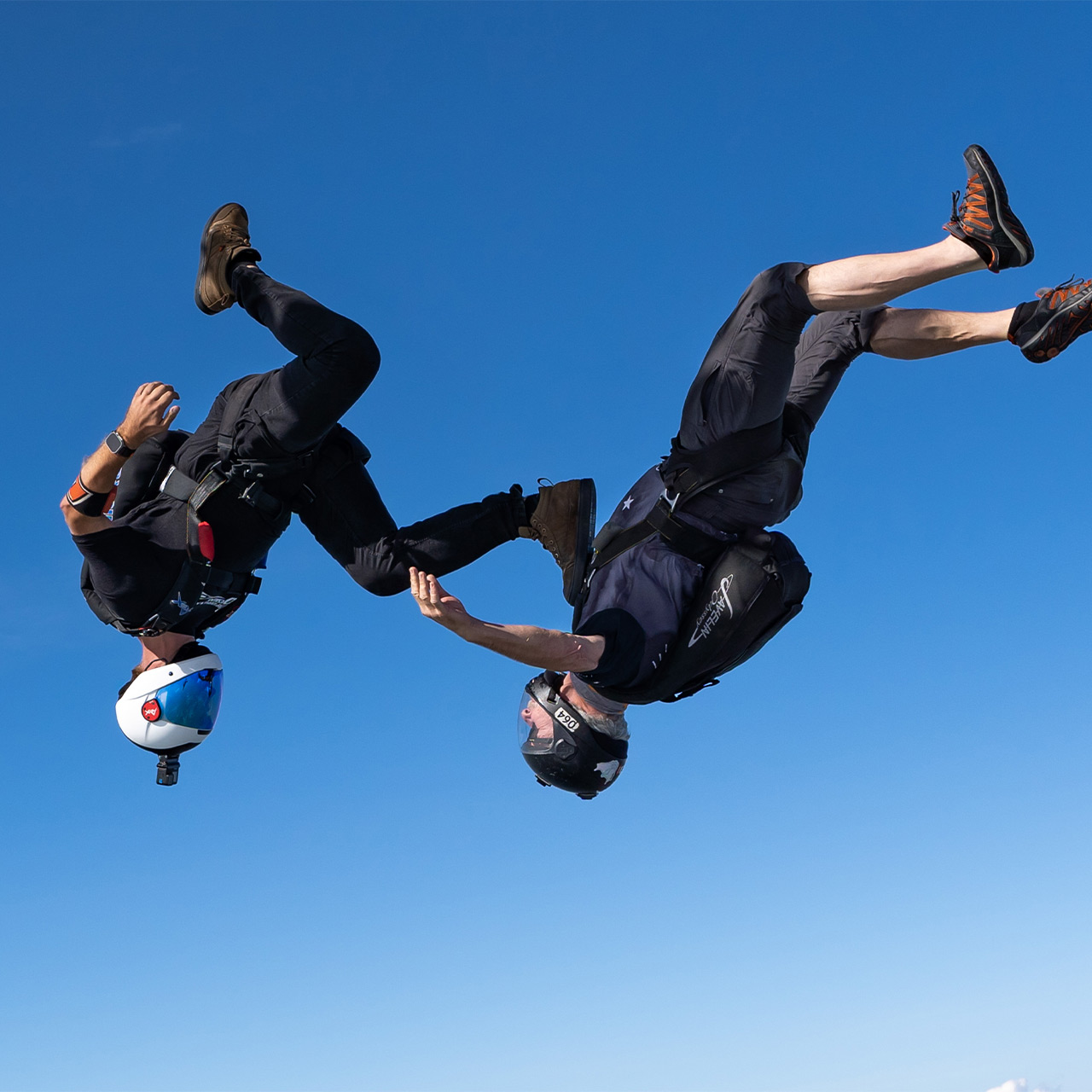 Two skydivers angle flying with one placing his food on the chest of the other simulating sky surfing
