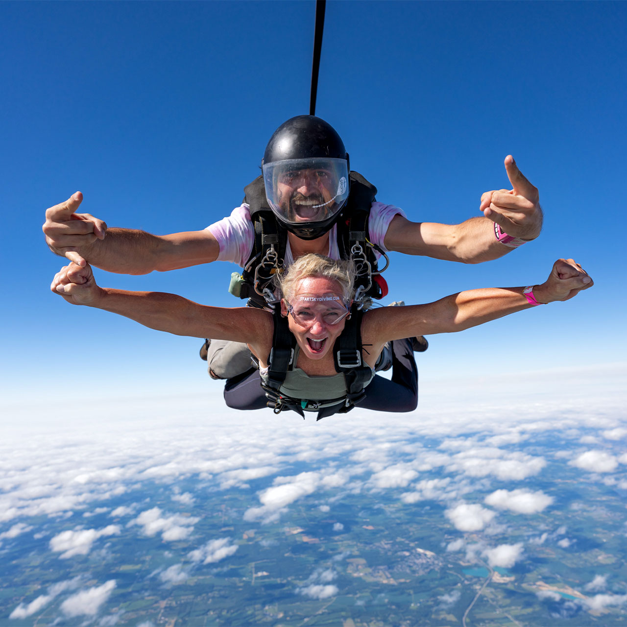 Tandem woman and her male instructor with arms outstretched during freefall.