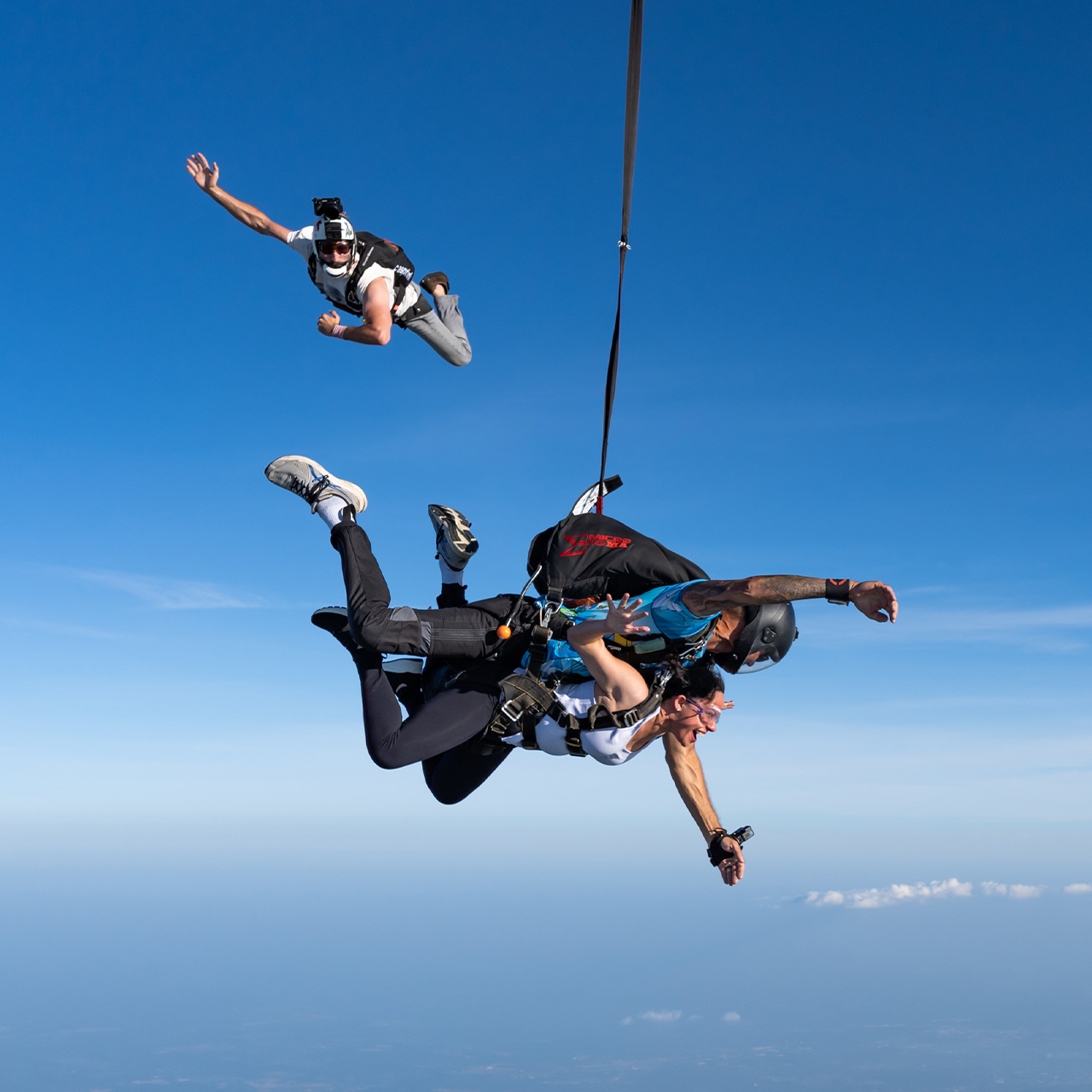 A tandem instructor and female passenger in freefall while a videographer flies around.