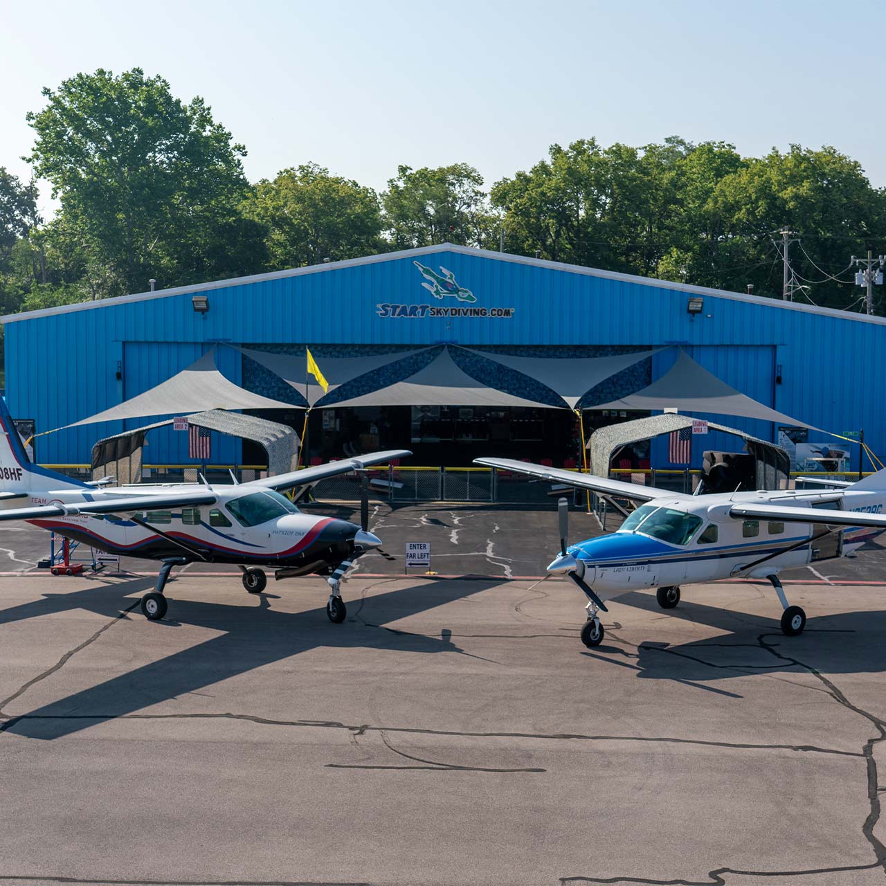 Start Skydiving's Cessna 208 Grand Caravan and Cessna 208B parked in front of a large, spacious blue airplane hangar