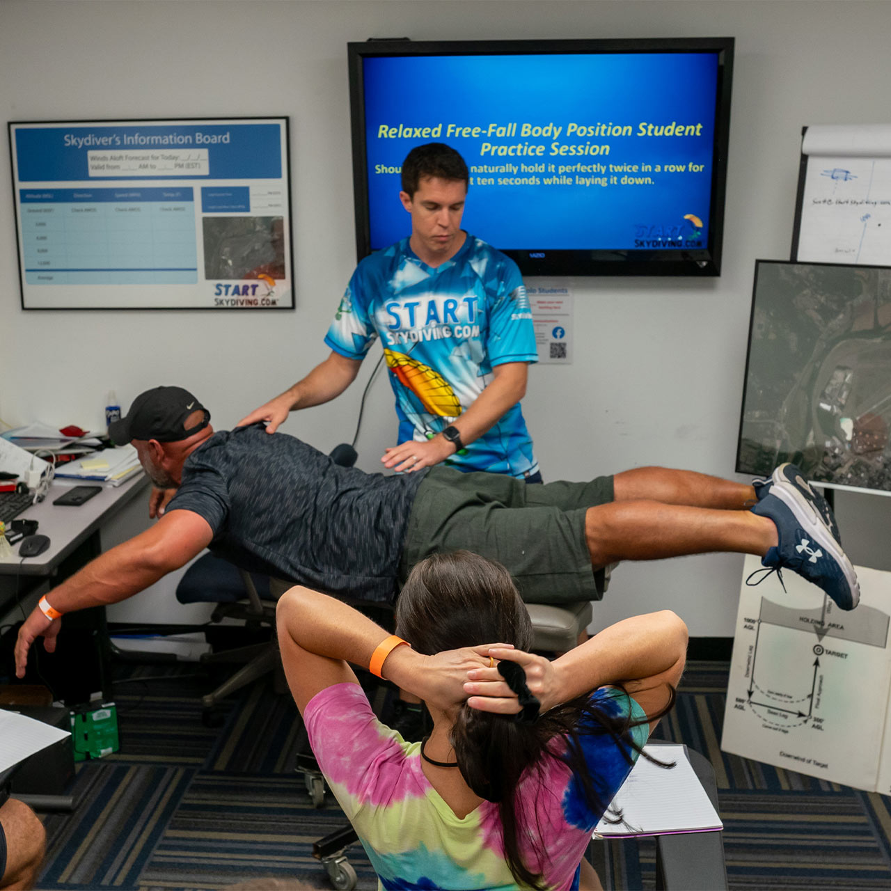 A skydiving student practices his relaxed freefall body position with the assistance of the instructor