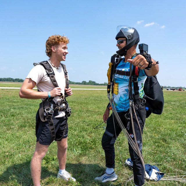 A red haired tandem student being interviewed by his tandem instructor moments after landing from a skydive at Start Skydiving